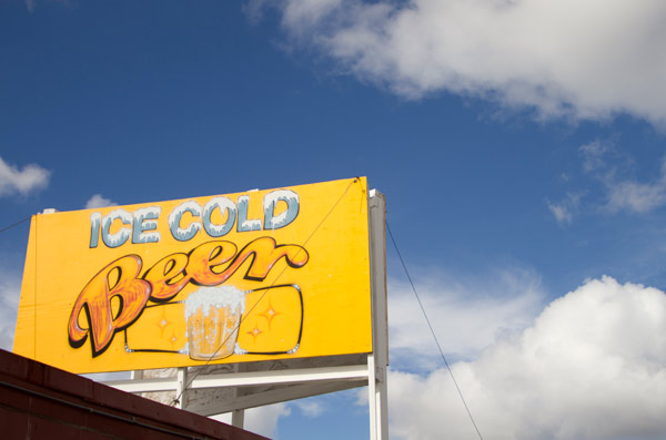 a sign for ice cold beer at the flea market with a bright blue cloudy sky behind it